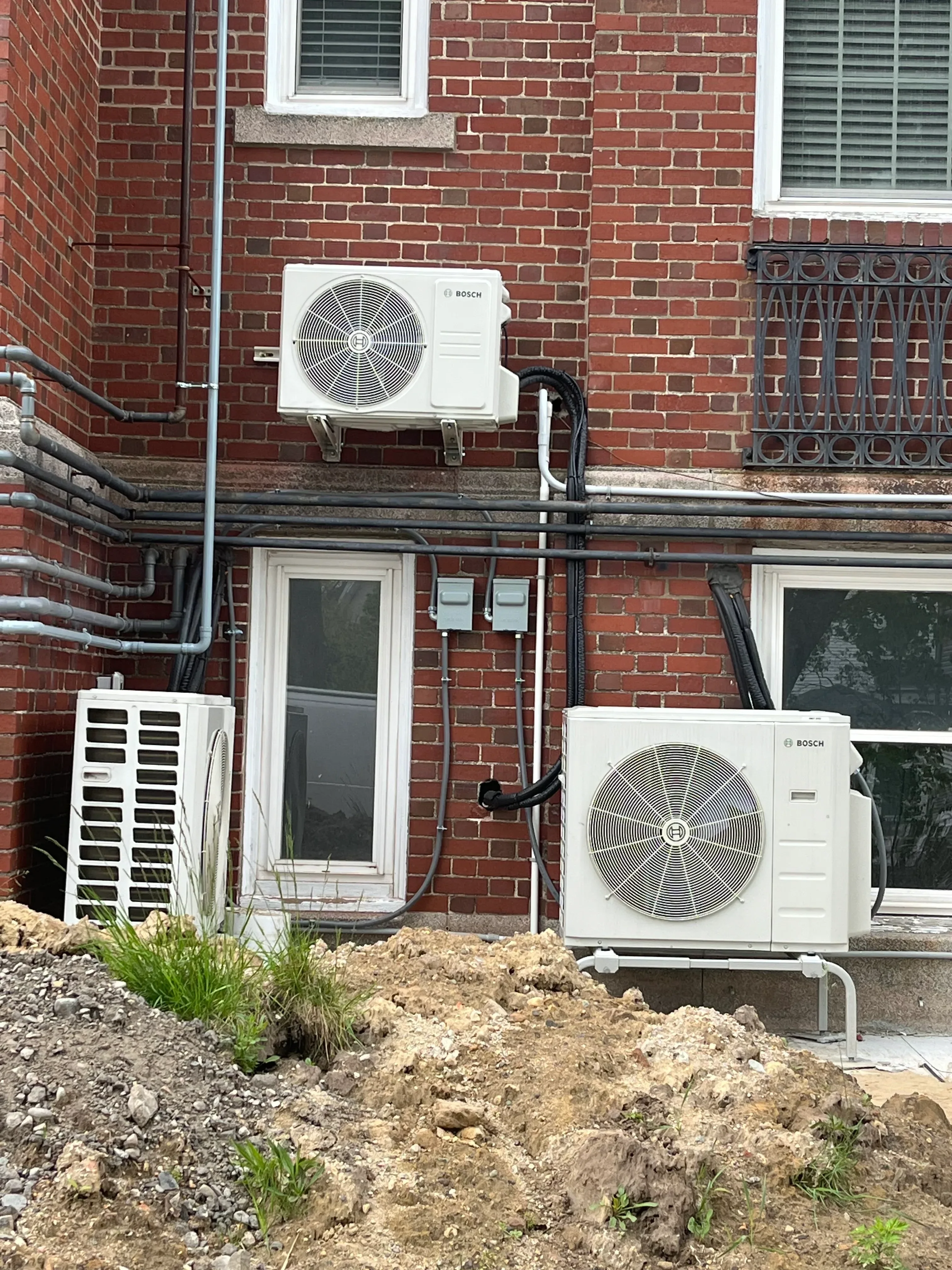 Two white Bosch heat pump condensers mounted on brick wall with black refrigerant lines and electrical connections