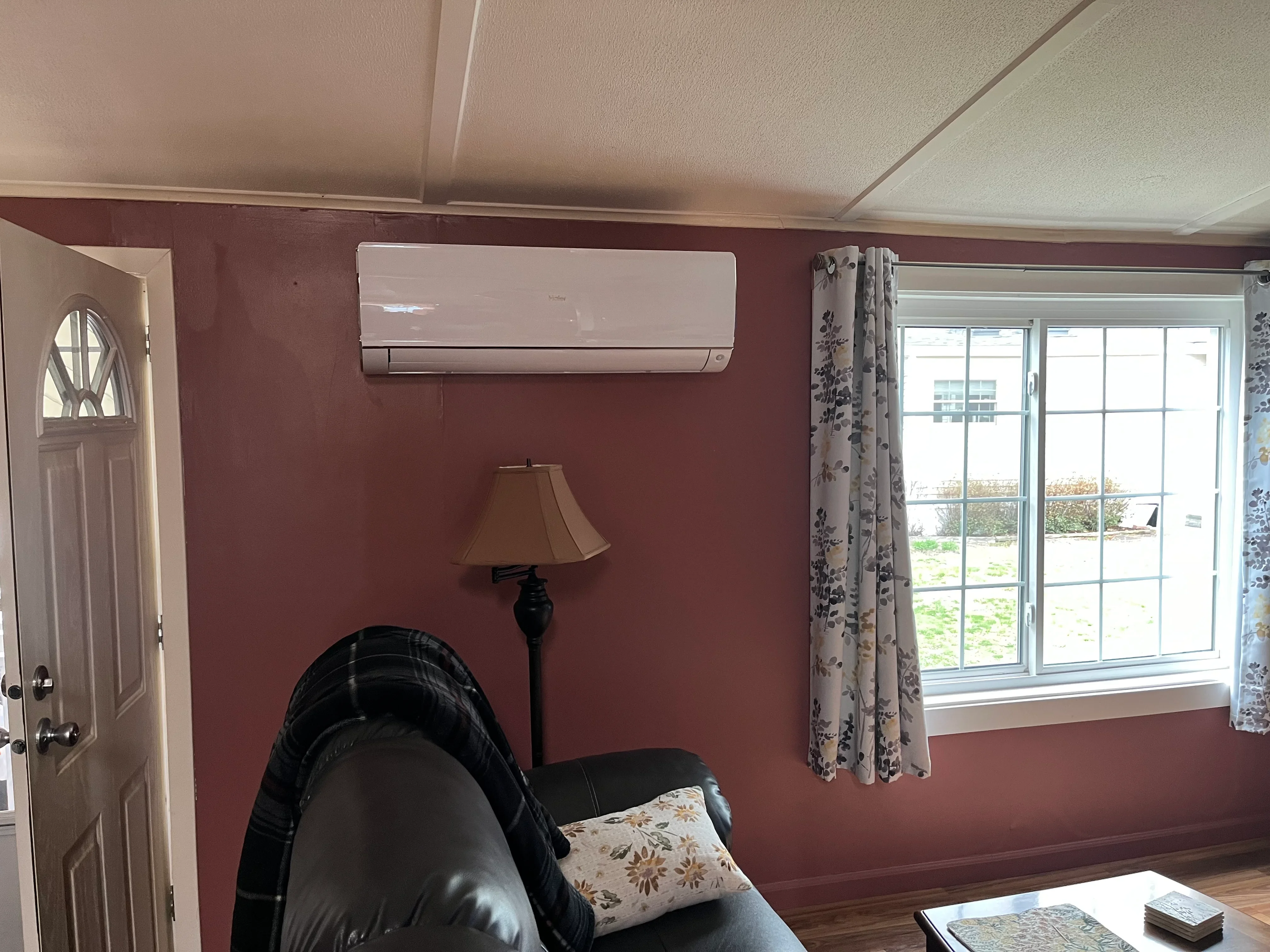 White ductless mini-split indoor unit mounted on burgundy wall above leather seating