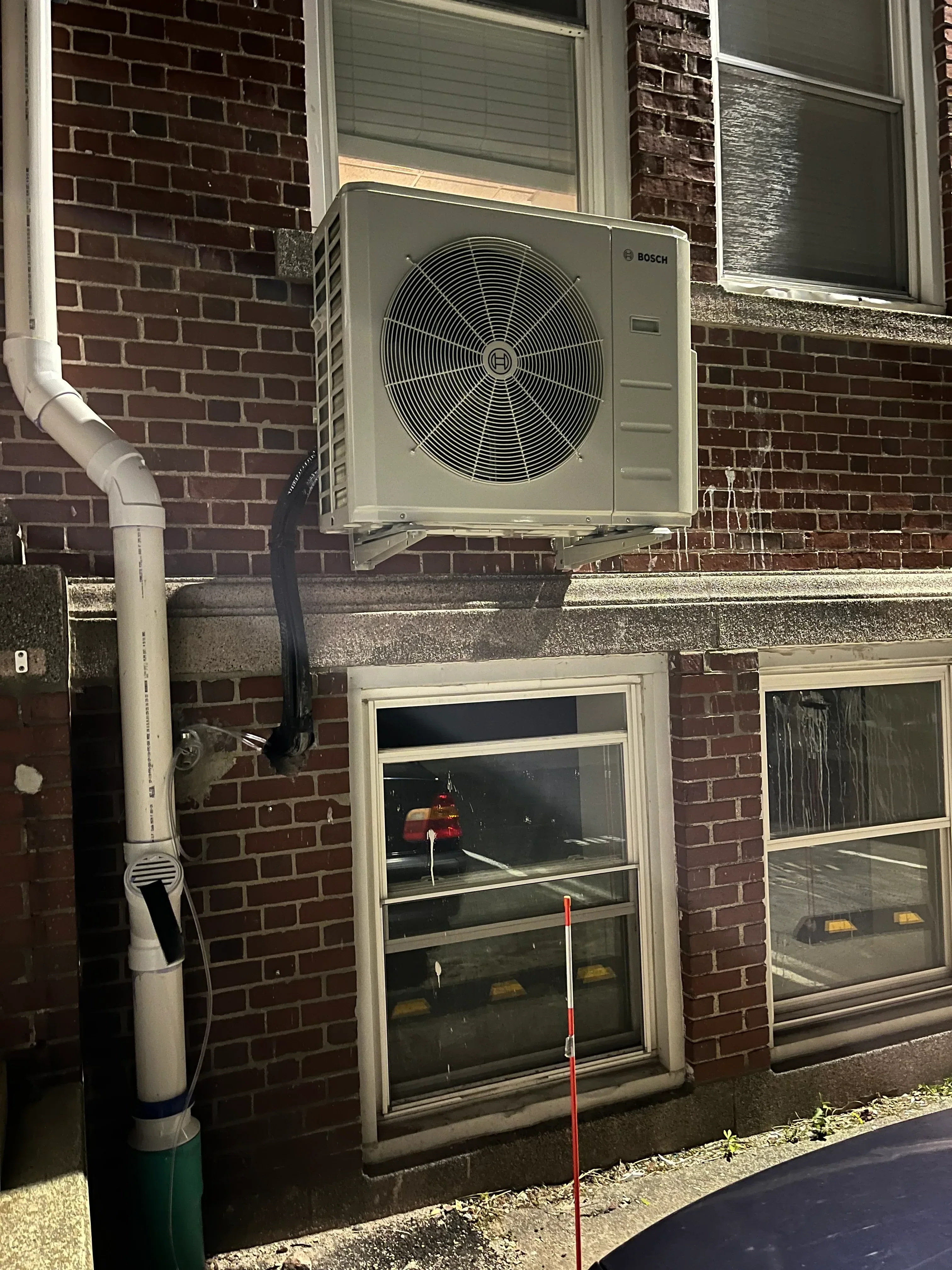 Bosch heat pump exterior unit mounted on brick wall with white condensate drain pipe