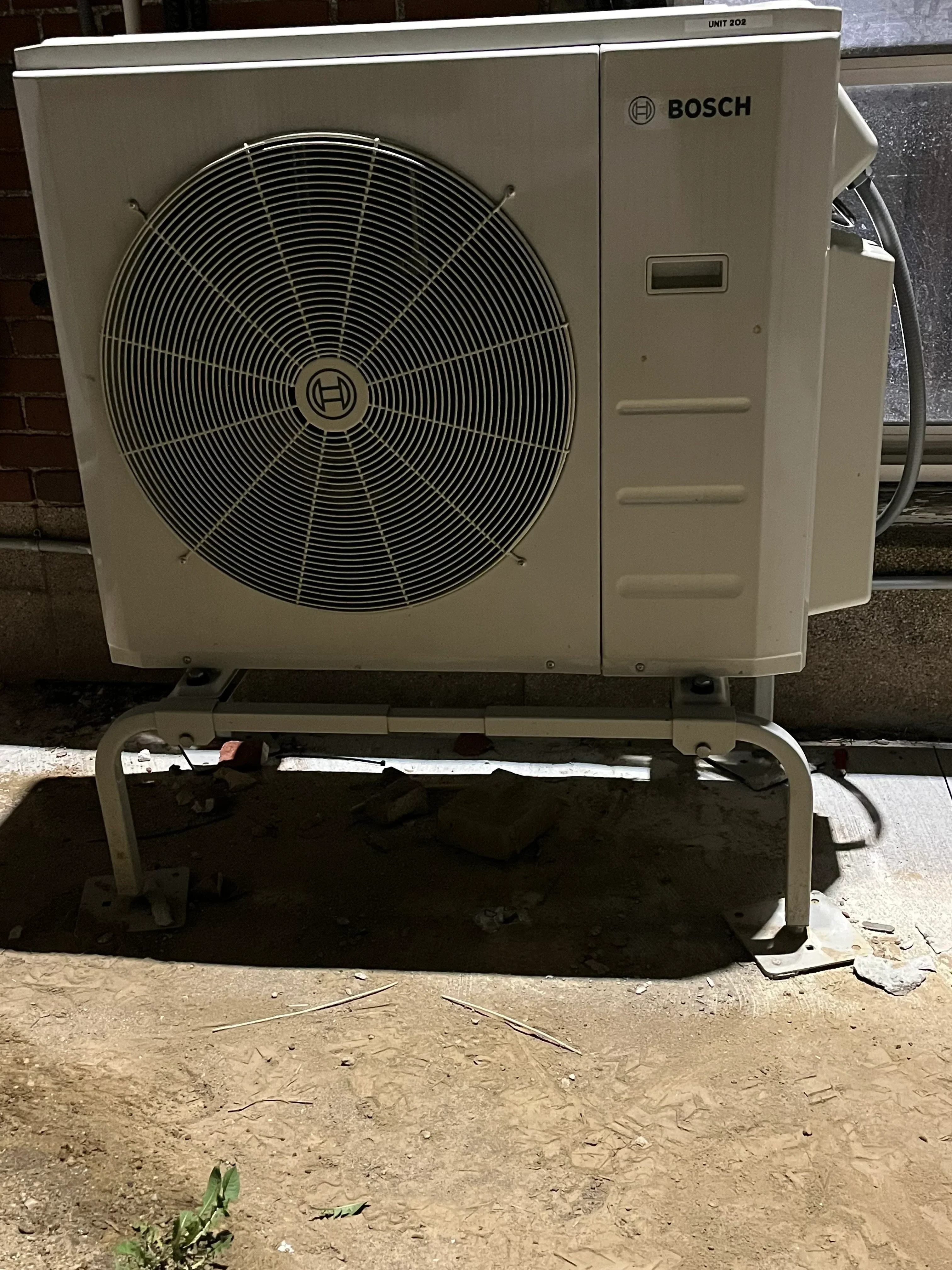 Bosch heat pump outdoor unit with black fan and beige casing, mounted on concrete foundation