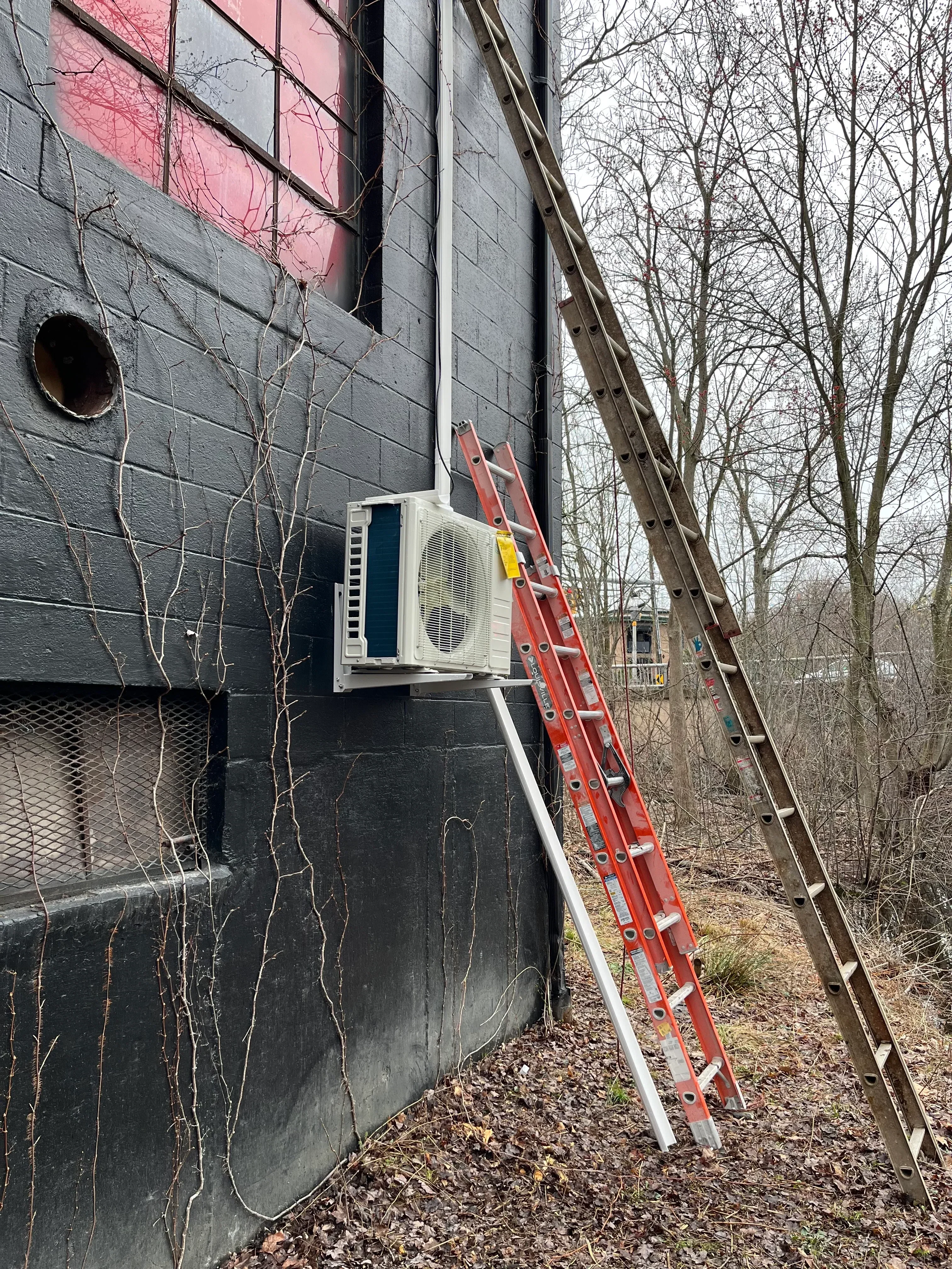 Rooftop AC unit installation with red extension ladder on slate and shingle roof