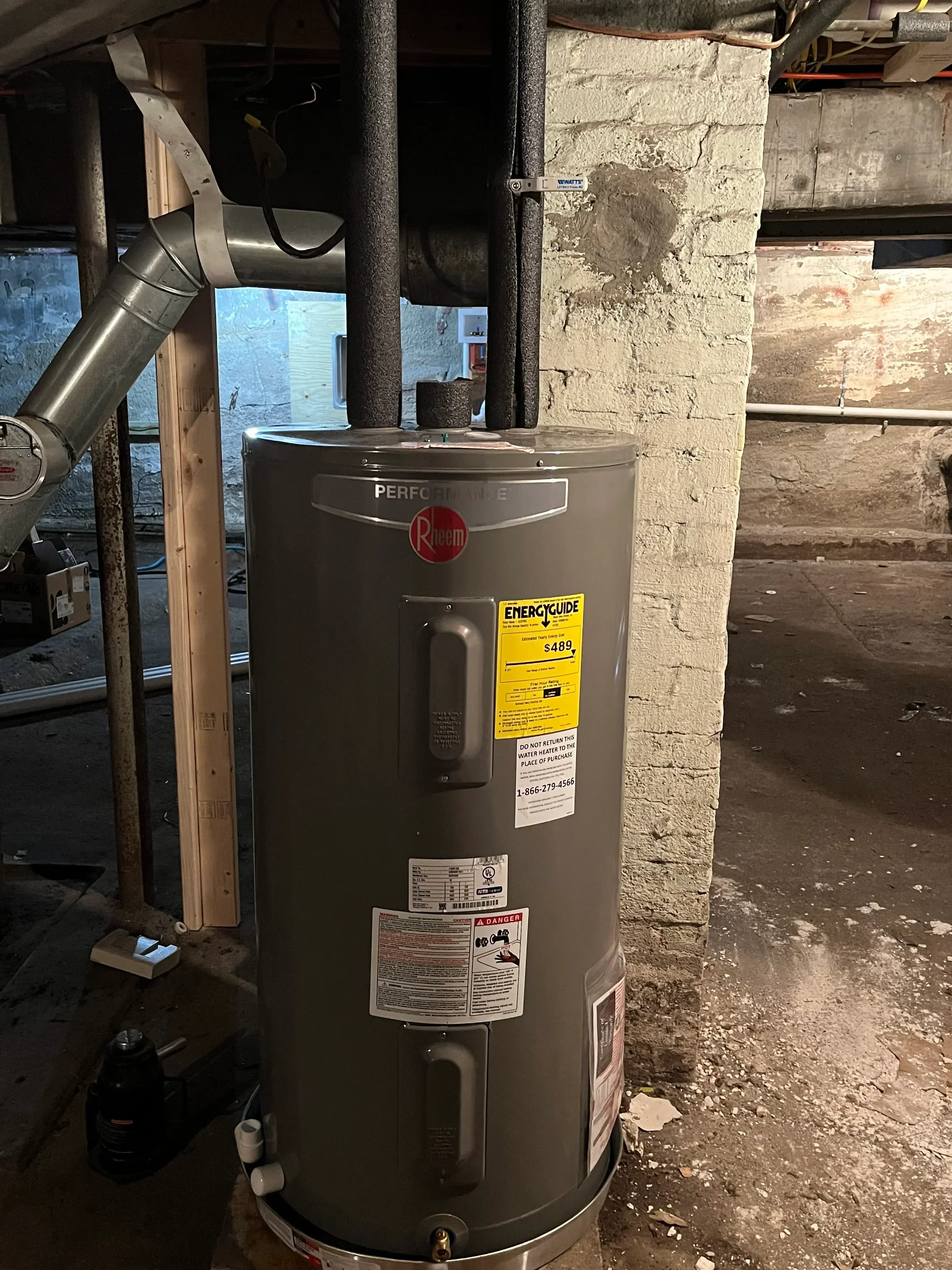 New water heater tank installation with copper piping and mounting hardware in basement