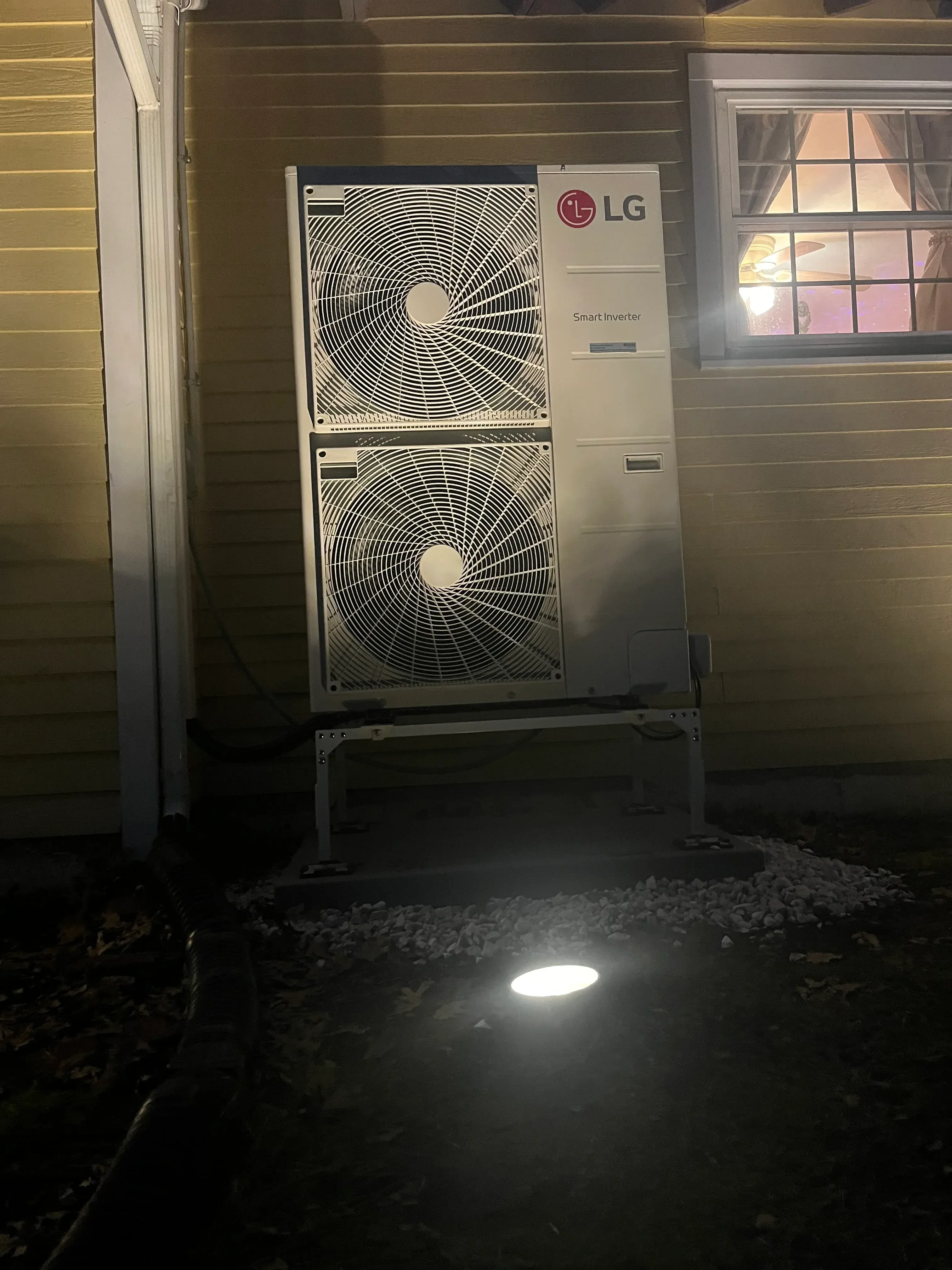 Dual-head LG heat pump with two condenser fans mounted on metal bracket against corrugated siding