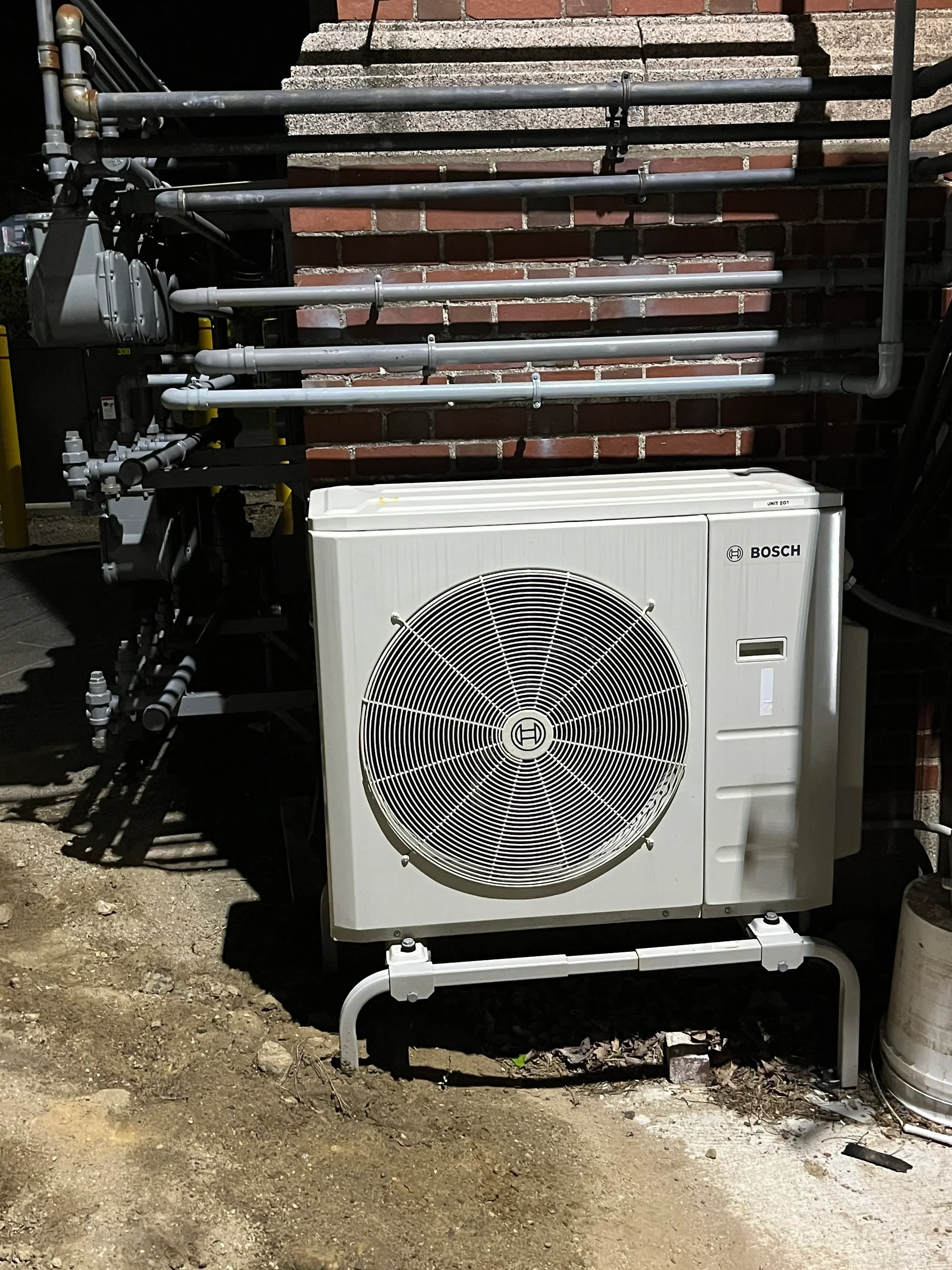 Bosch heat pump unit with copper piping, white casing, and metal protective cage installed outdoors