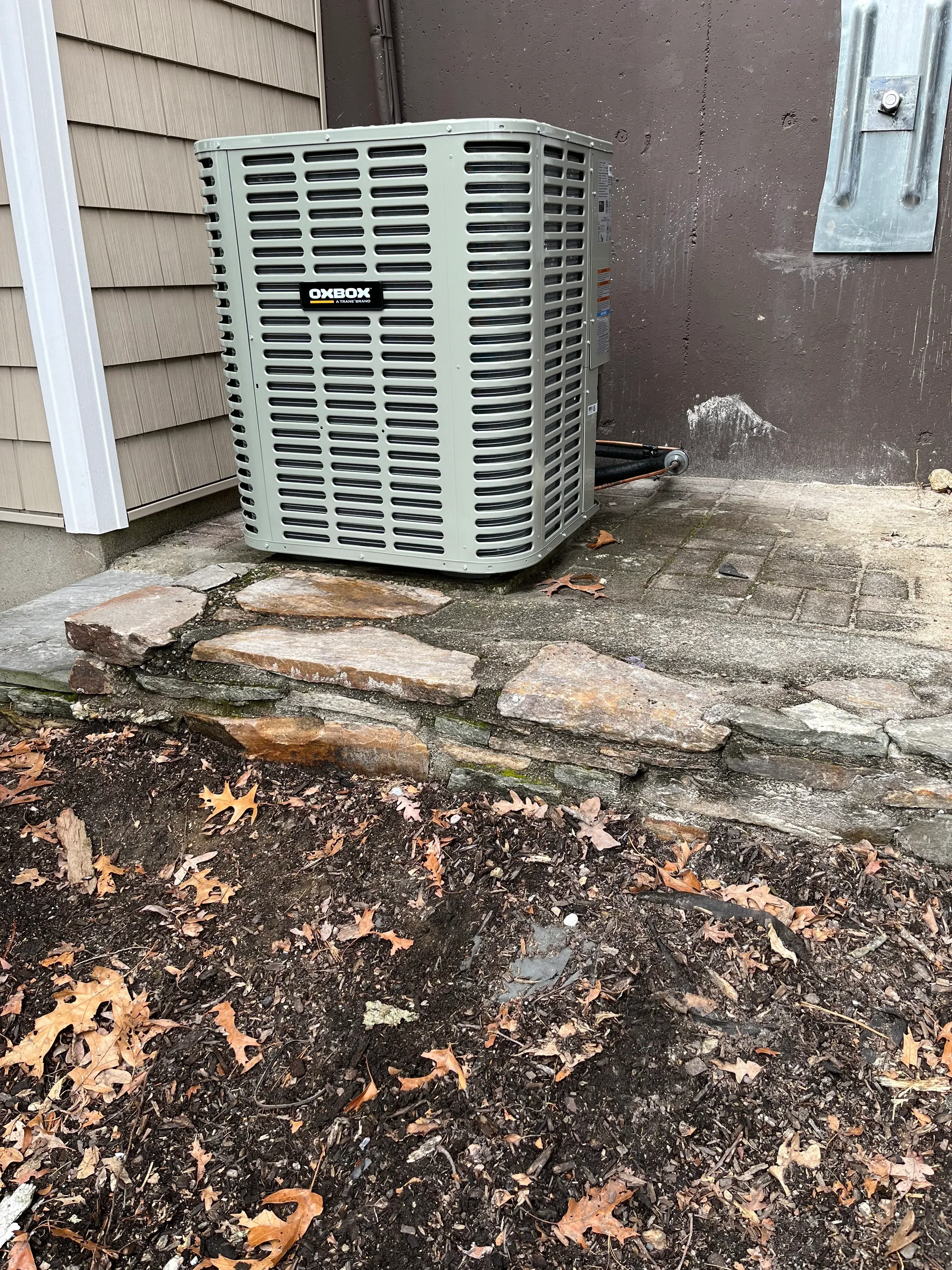 White AC condenser unit installed on concrete pad next to foundation wall