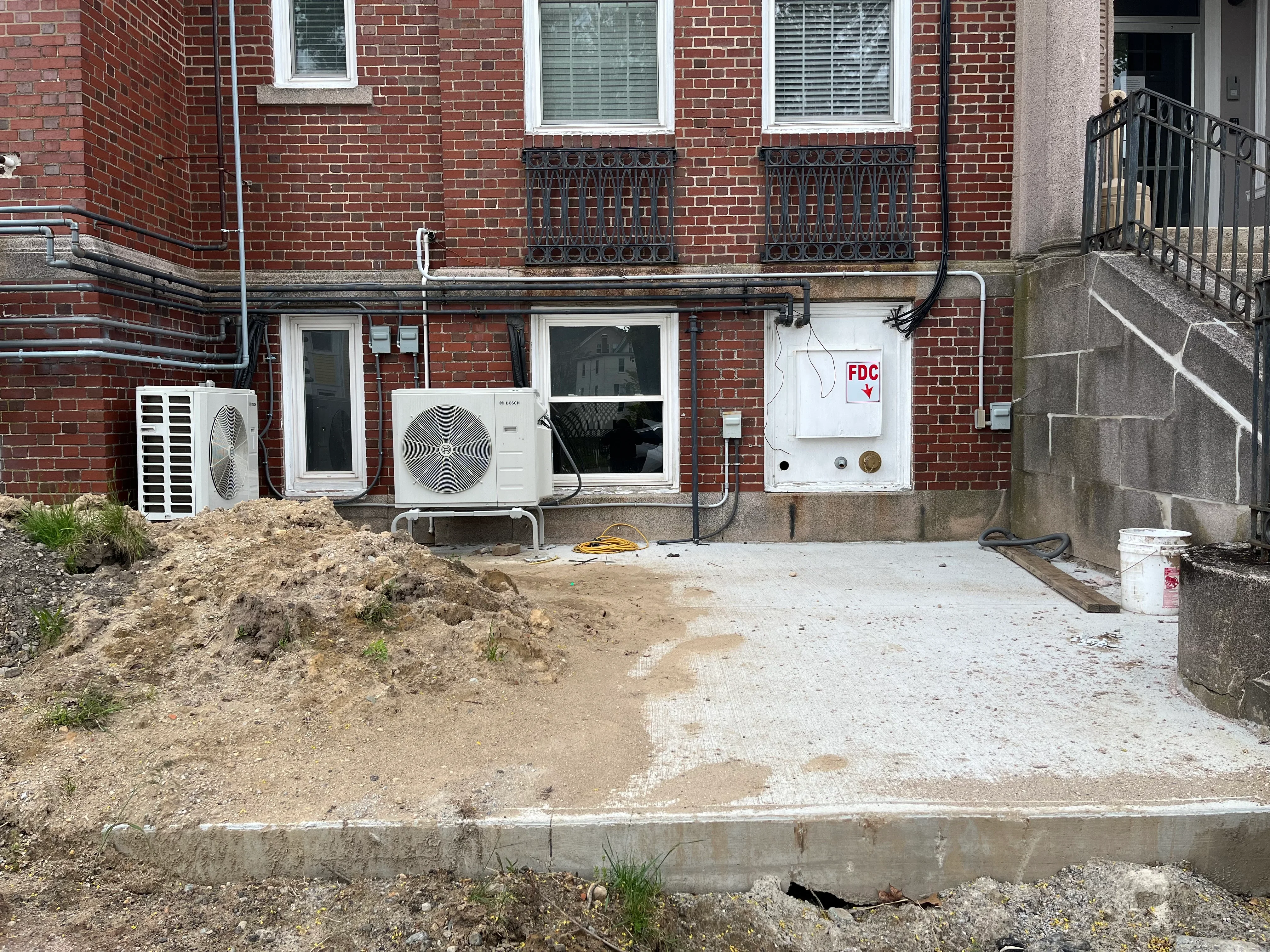 Heat pump outdoor unit installation with refrigerant lines and electrical connections on brick building foundation