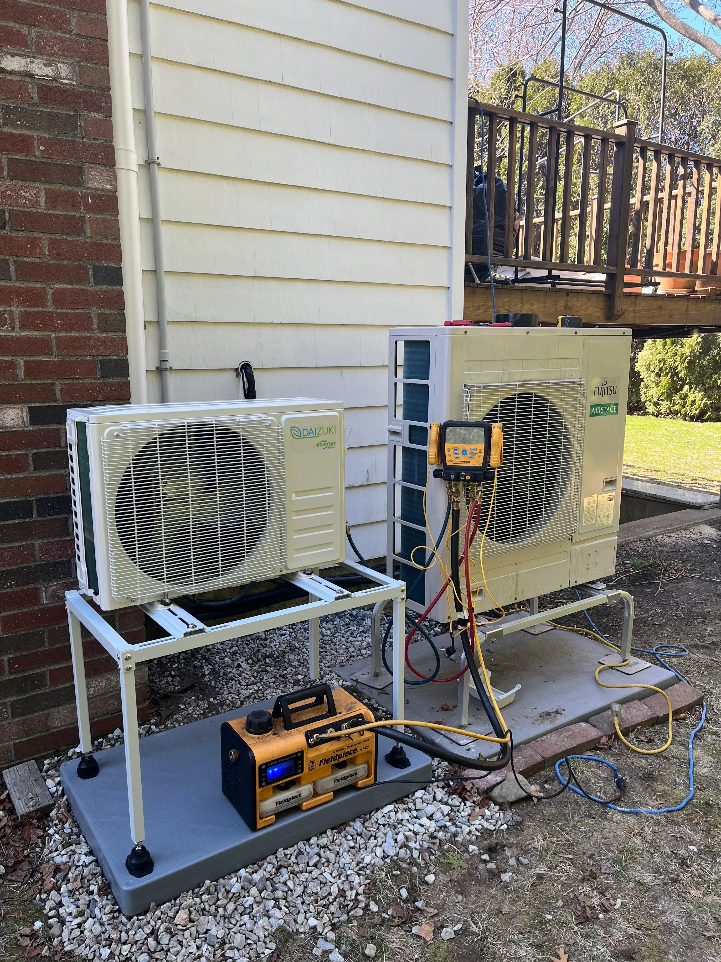 Two heat pump units installed outdoors with electrical connections, testing equipment, and copper refrigerant lines